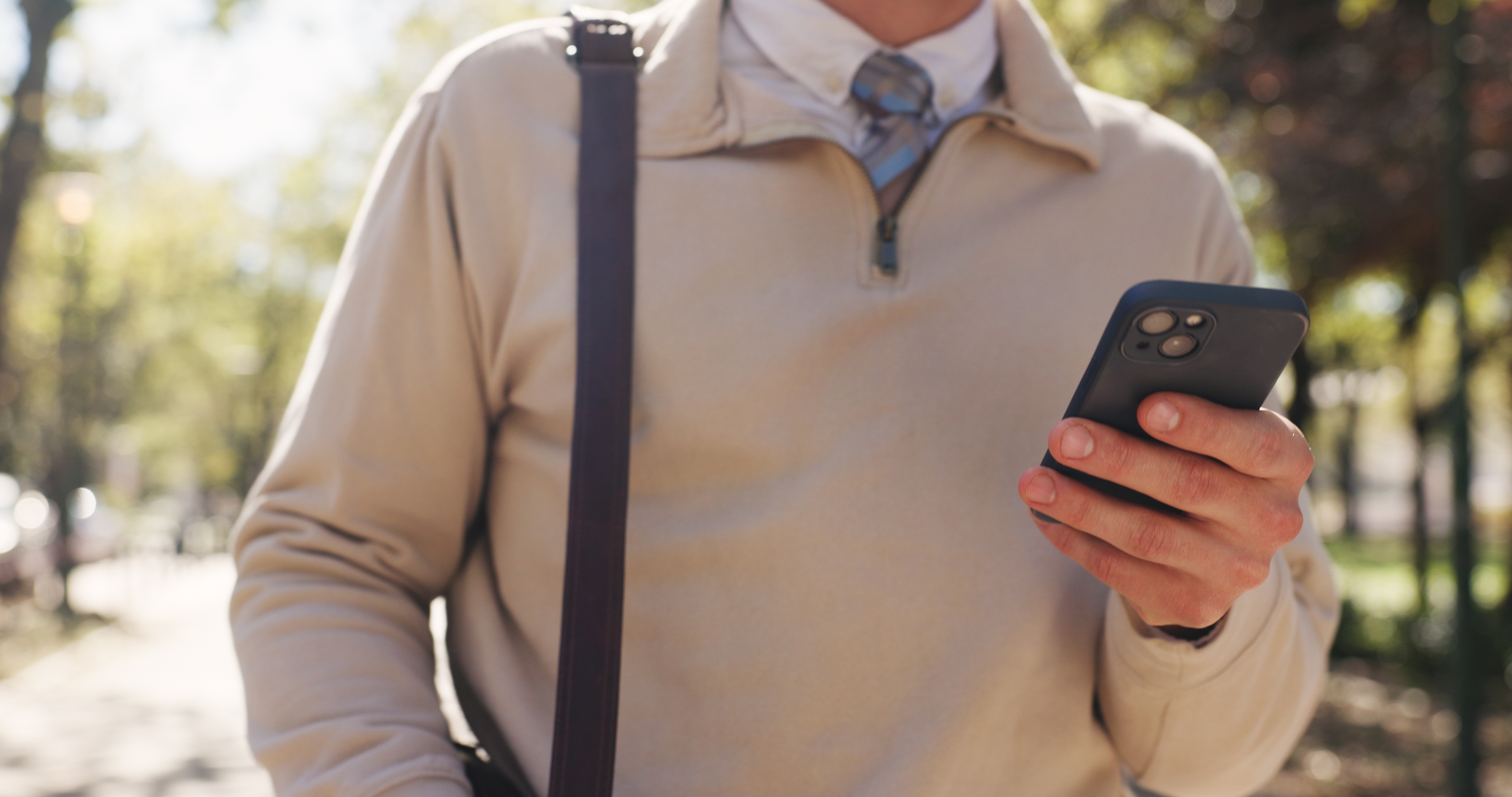 Professional using an iPhone outdoors to stay connected to work.